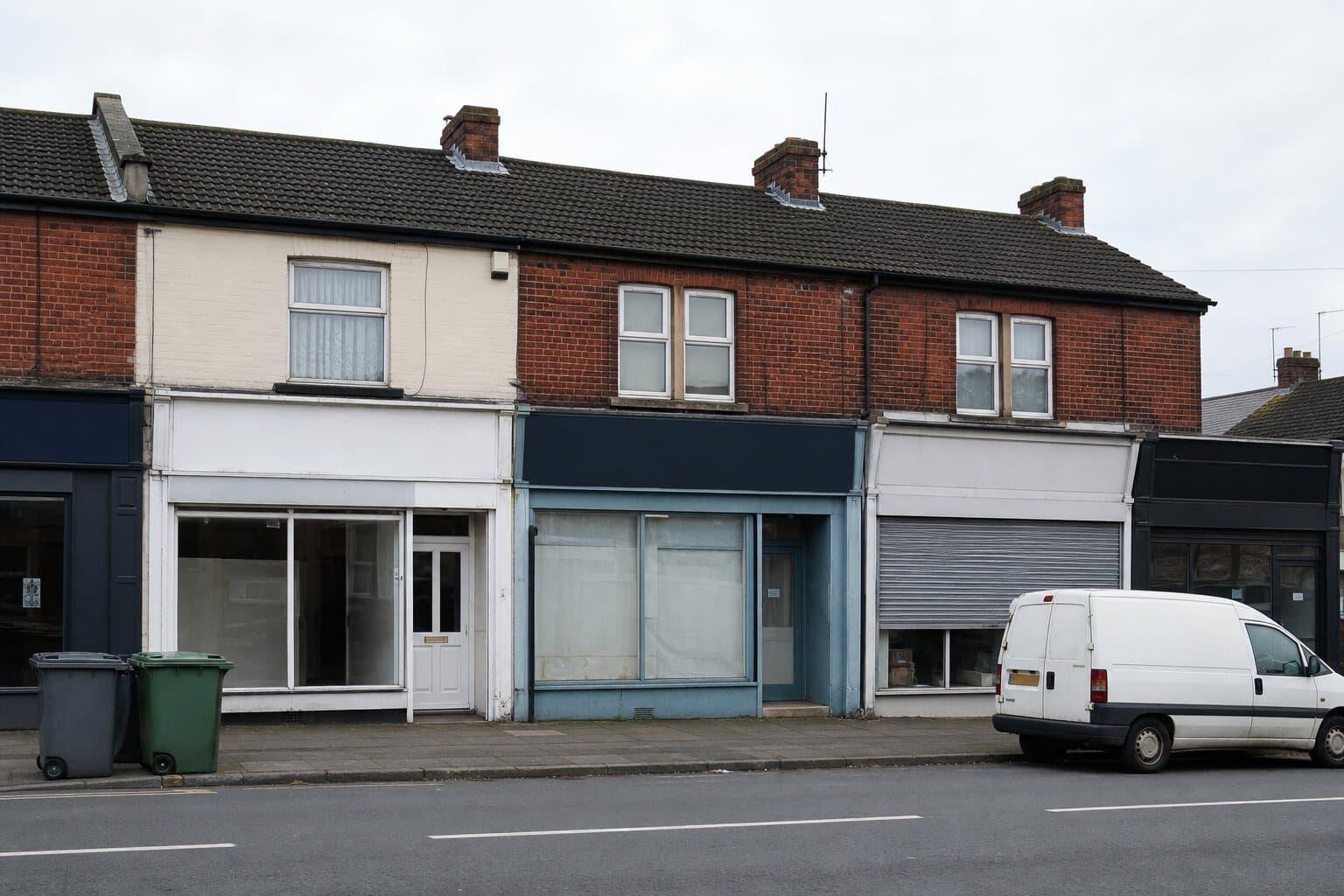 A row of small independent shopfronts on a modest high street, with a van parked at the kerb.